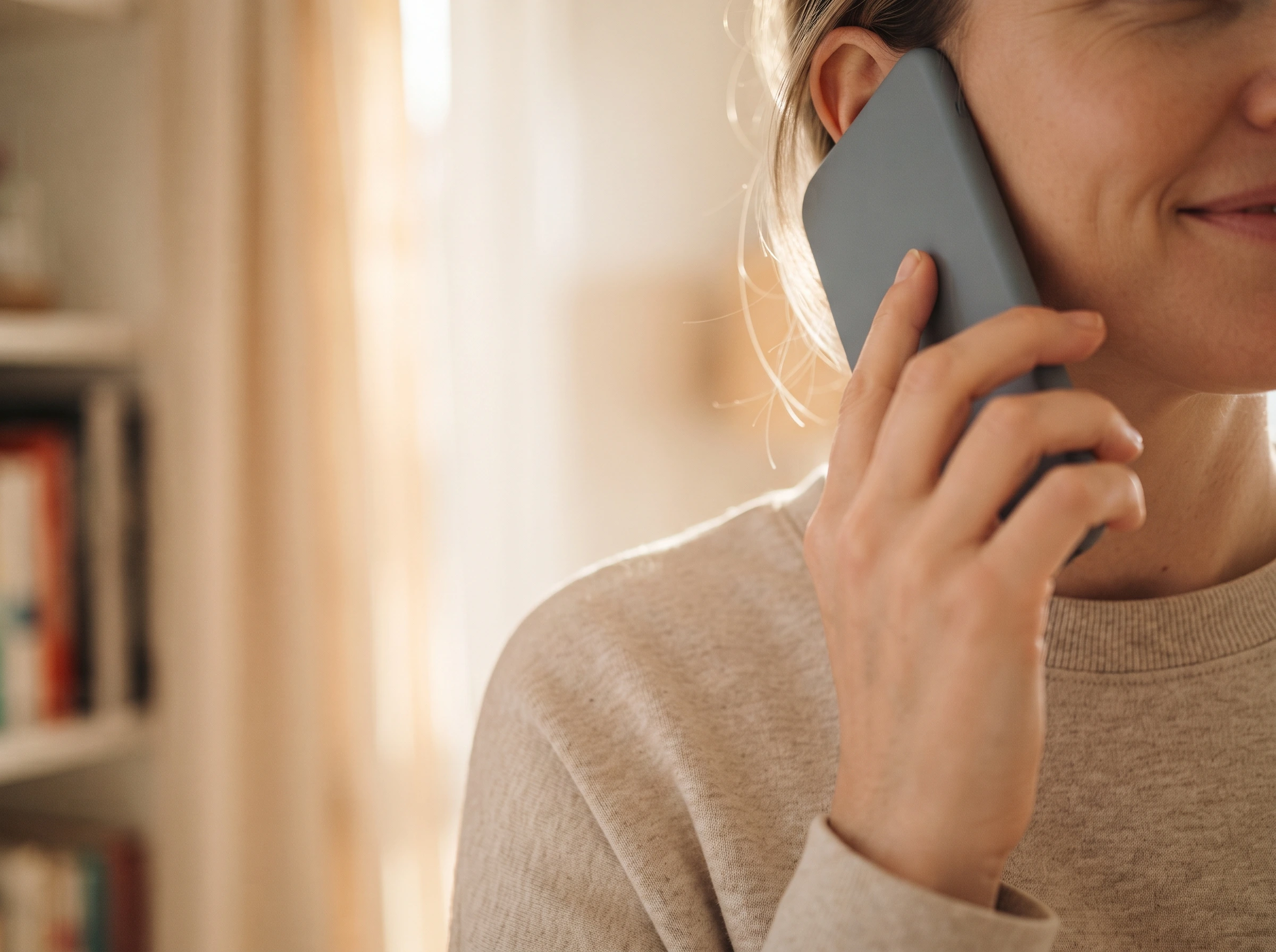 A warm side portrait of a person holding a smartphone to their ear, listening in a softly lit living room